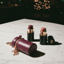 Two lipsticks with rose gold caps and a matching case on a marble surface.