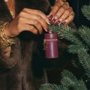Person decorating a Christmas tree with a purple ornament, wearing a gold bracelet.