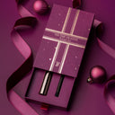 Mascara and eye liner holiday gift set on a purple background with a decorative box with 'Tis the Season' text 