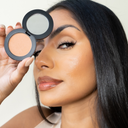 Concealer compact with light peach concealer on open case beside woman’s face
